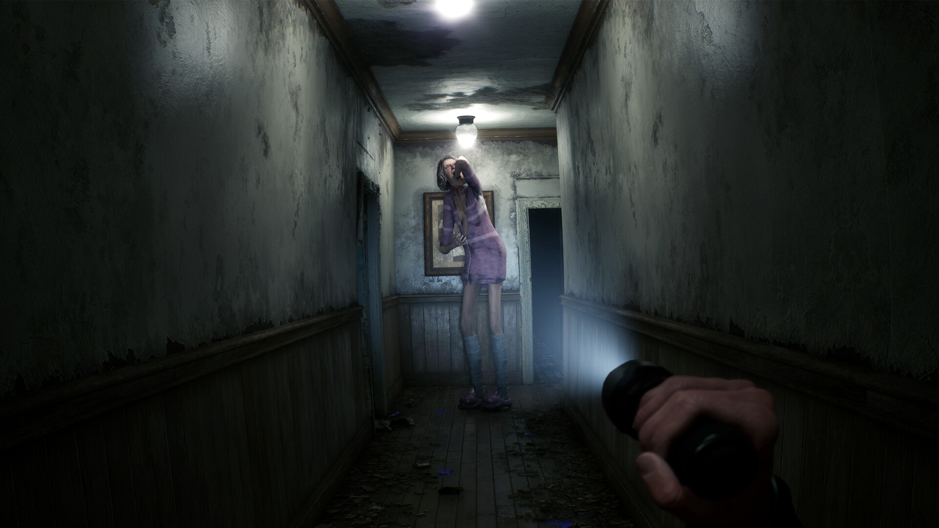 The player searches a dark hallway with a handheld light while a figure blocks the route.